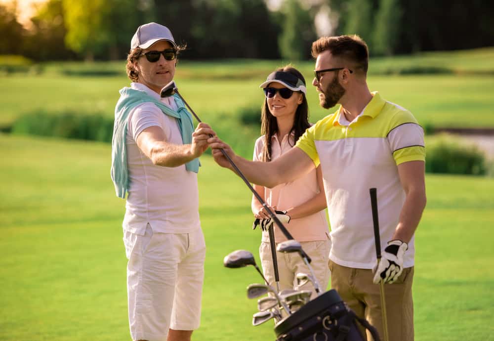 Two men and a woman are choosing golf clubs