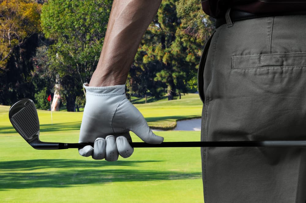 male golfer on a golf course holding a six iron behind his body