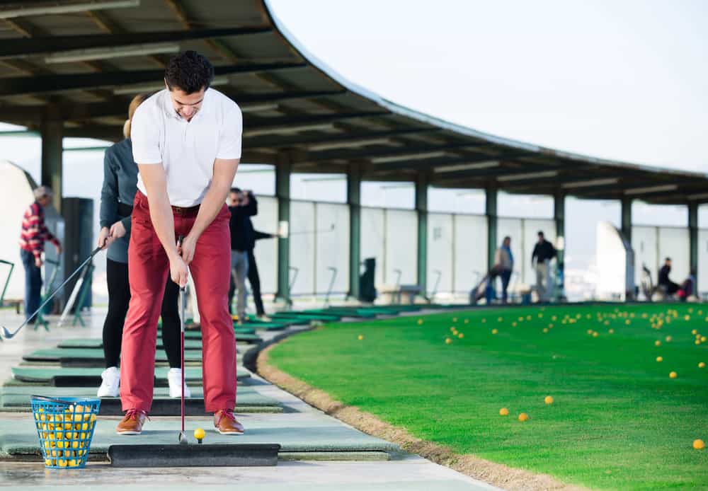 smiling man playing golf is going to hit ball at golf course