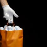 Close-up of a hand wearing a golf glove holding a bag full of golf balls