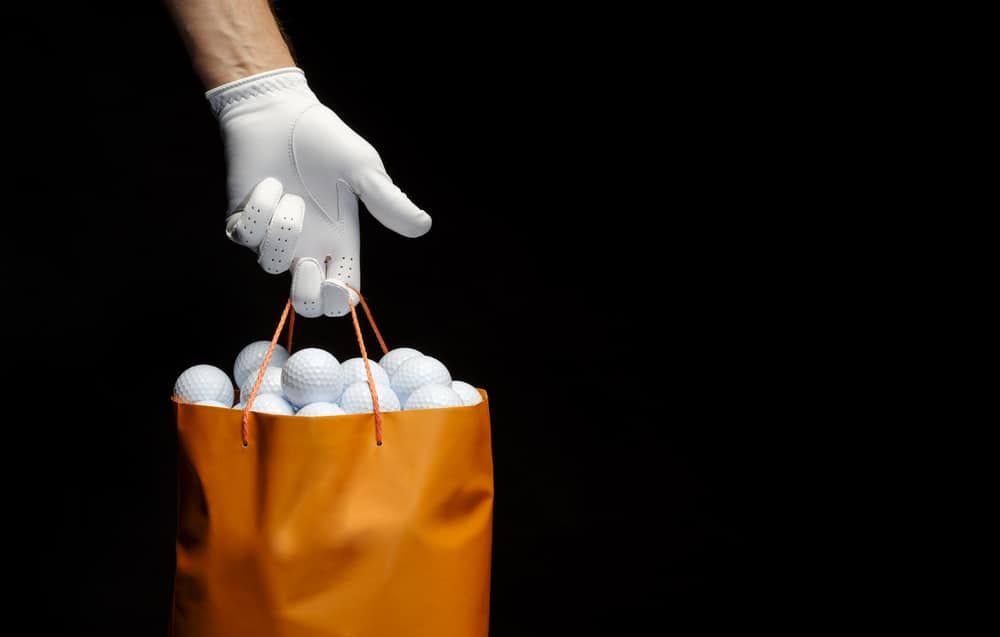 Close-up of a hand wearing a golf glove holding a bag full of golf balls