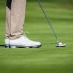 Close up of a male golf player with white shoes putting on green