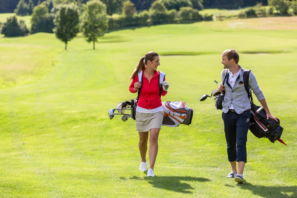 Couple carrying golf bag while walking on golf course