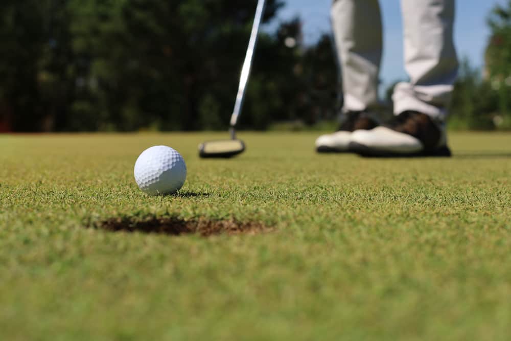 Golf player at the putting green hitting ball into a hole