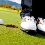 Golf player hitting the ball close-up on shoes