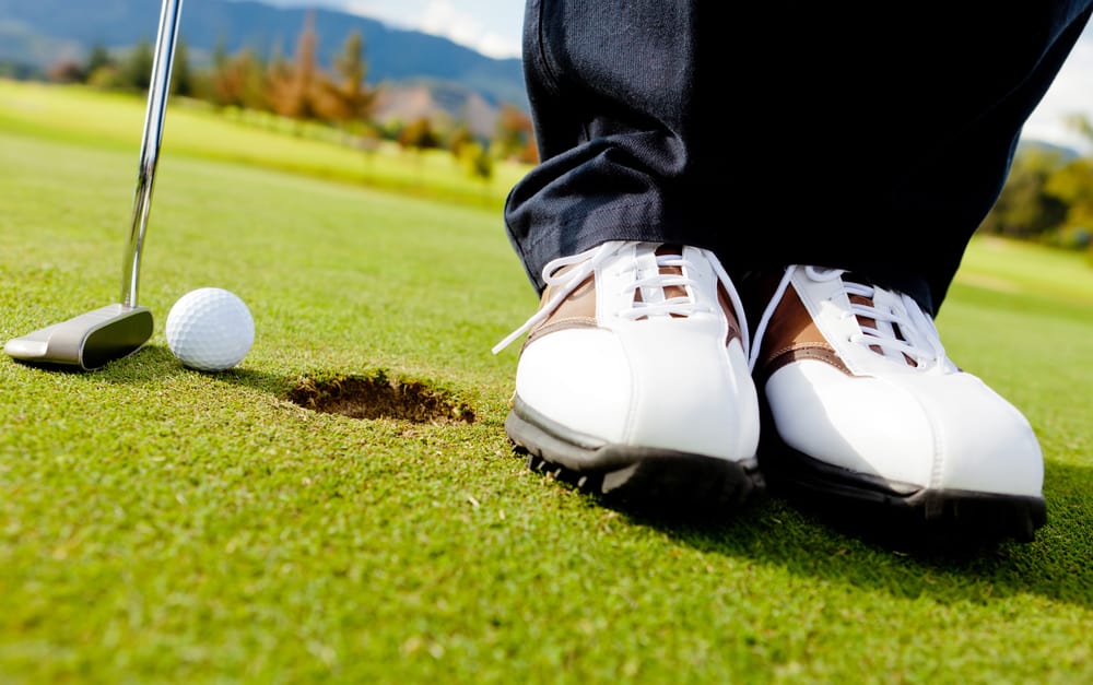 Golf player hitting the ball close-up on shoes