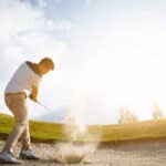 Golfers exploding sand in the bunker