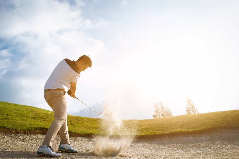 Golfers exploding sand in the bunker