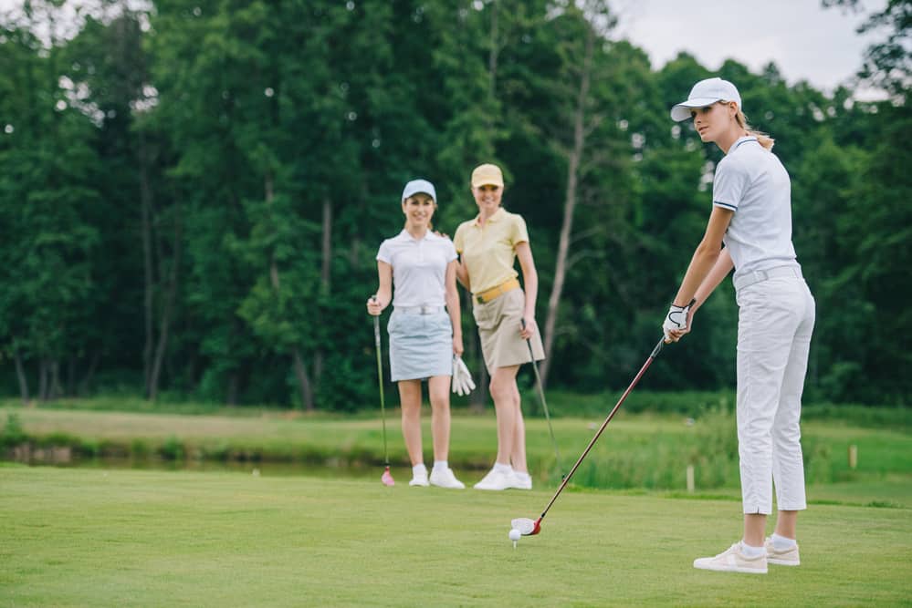 Selective focus of woman in cap playing golf while friends