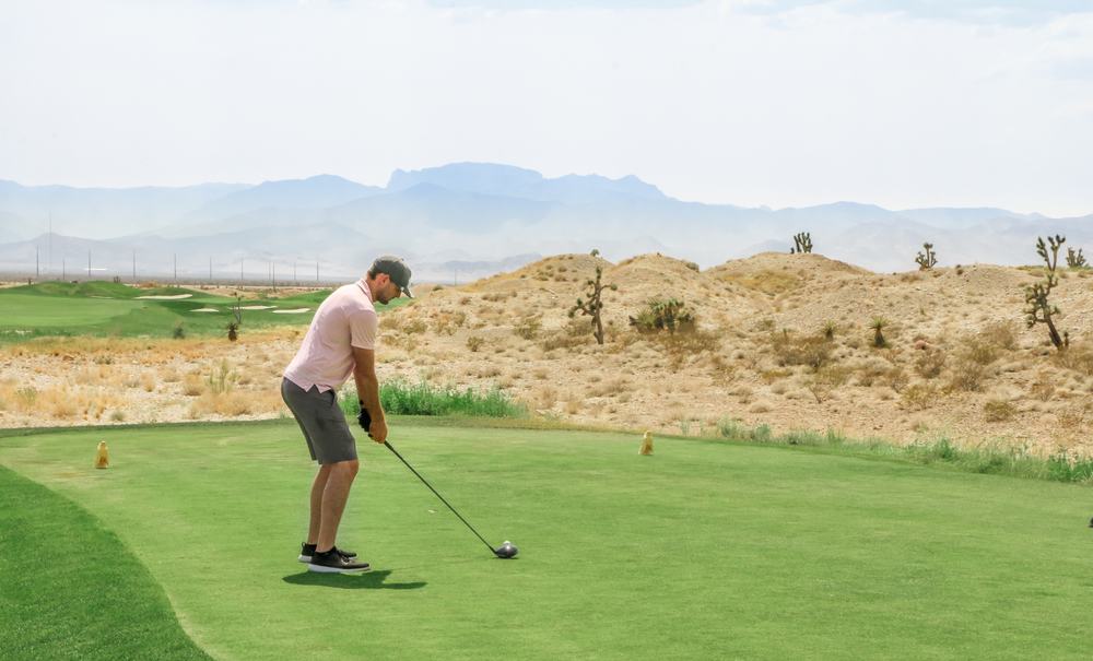 a golfer teeing off with a mountain view in the distance