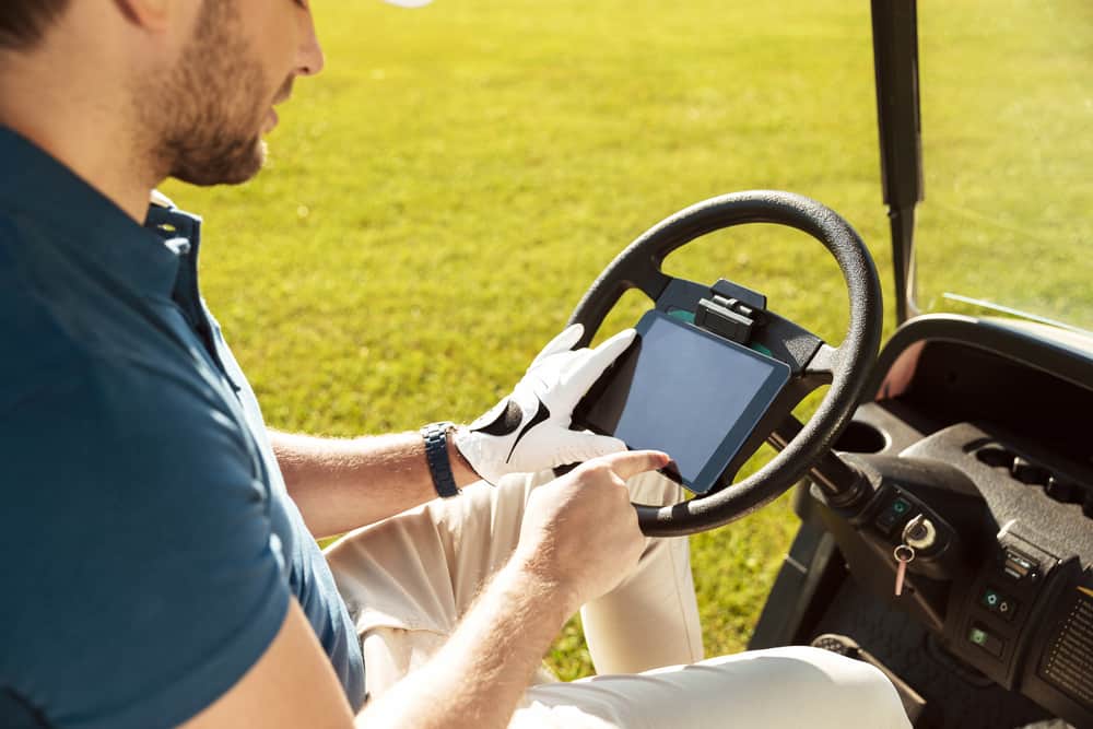 male golfer sitting in a golf cart and using tablet computer