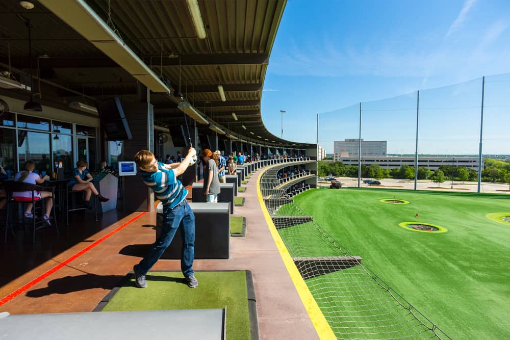 man hits a golf ball at a Top Golf golfing complex