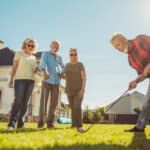 Group of senior friends having fun playing mini golf at the backyard lawn