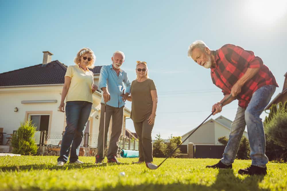 Group of senior friends having fun playing mini golf at the backyard lawn