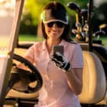 woman is using a smart phone and smiling while driving a golf cart