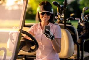 woman is using a smart phone and smiling while driving a golf cart
