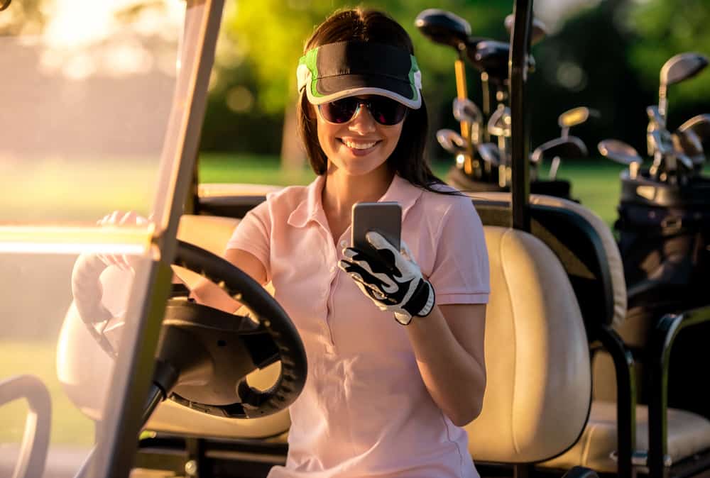 woman is using a smart phone and smiling while driving a golf cart