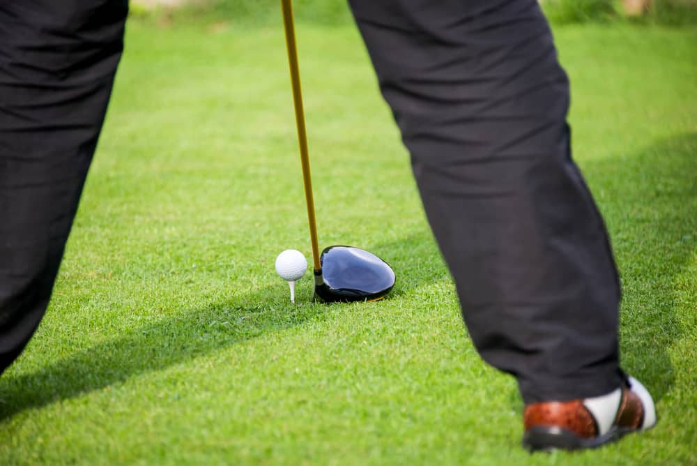 golfer addresses golf ball with driver in tee box