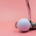 Golf ball with putter are on pink background