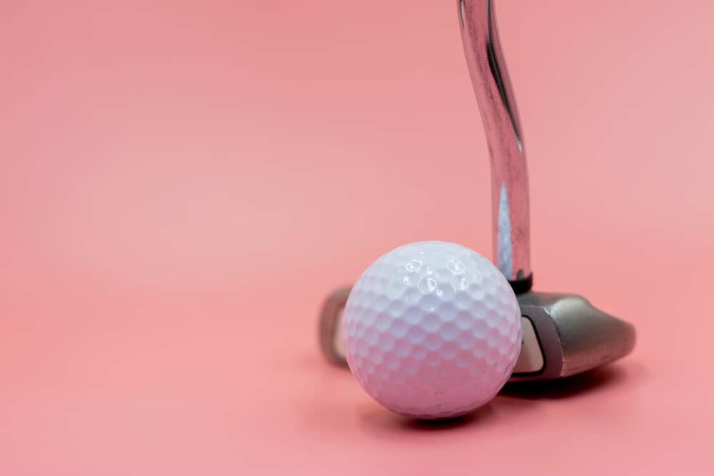 Golf ball with putter are on pink background