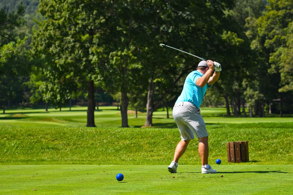 Young Man on Golf Course Hitting an Iron off the Tee