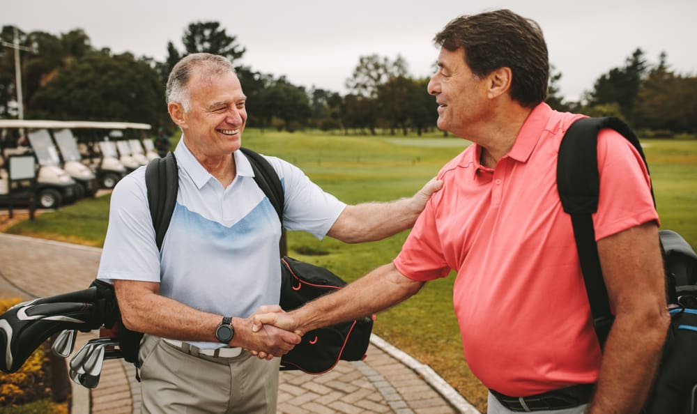 men are shaking hands and smiling when meeting on a golf course