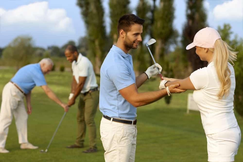 Female golfer learning golfing, male instructor helping.