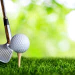 Golf club and golf ball on tee onto the green grass ready to be shot