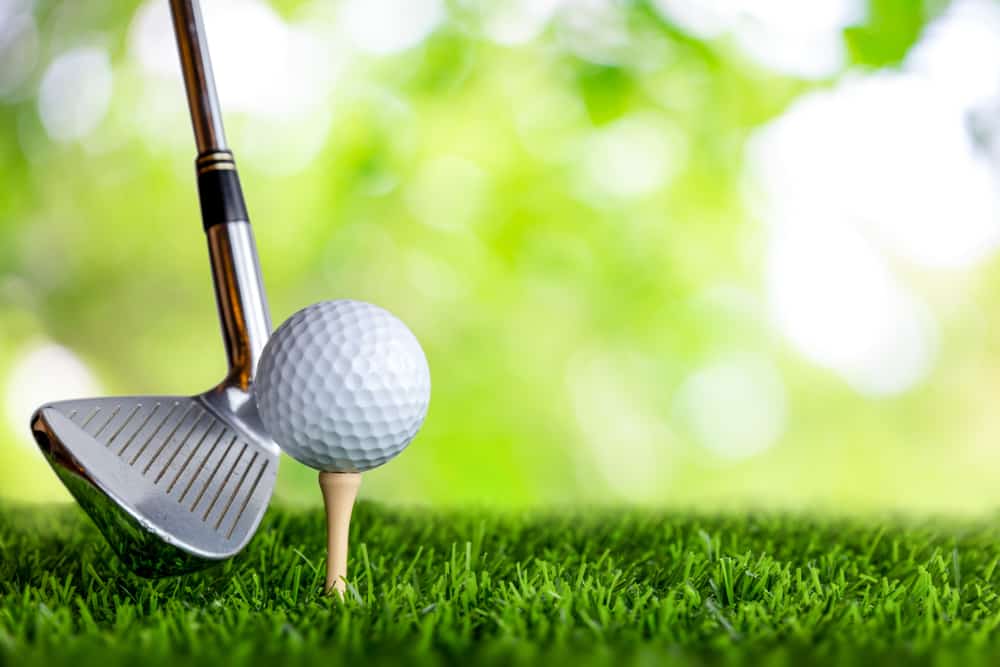 Golf club and golf ball on tee onto the green grass ready to be shot