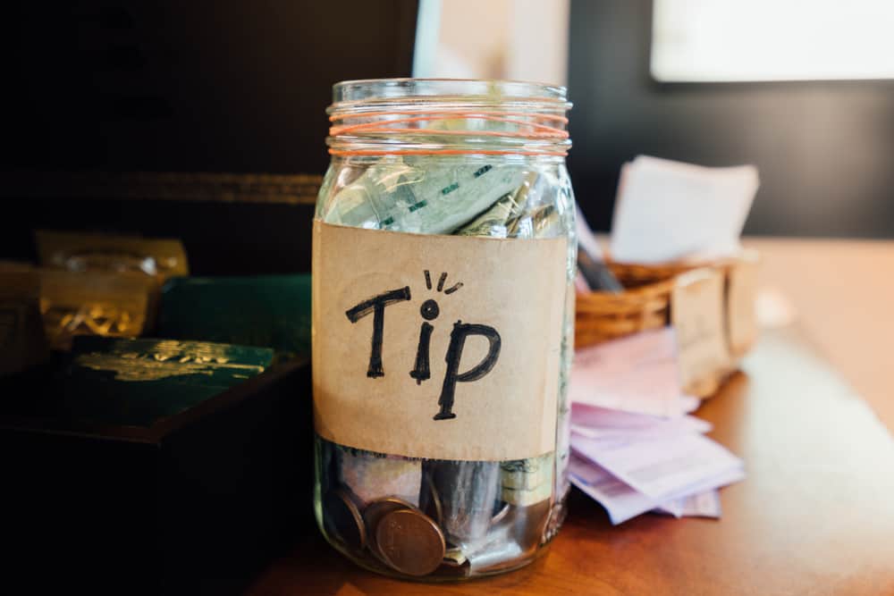 Tip box, money bank and coins in the vintage glass on wood counter in cafe