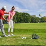 Young female athlete practicing a golf swing on the course helped by a skilled instructor