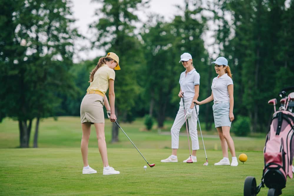 Woman in cap playing golf while smiling friends