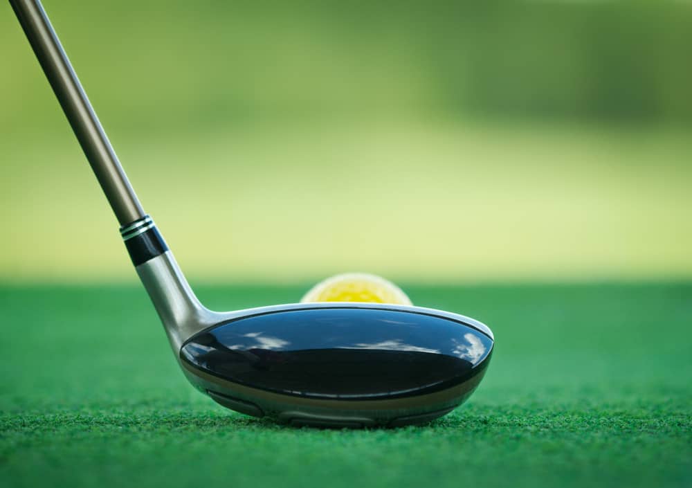 Golf ball behind hybrid club at driving range