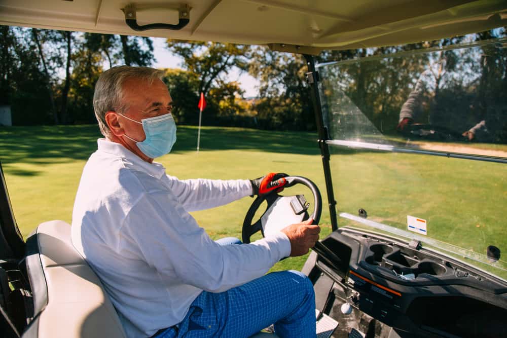 Senior golfer with disposable face mask driving his golf buggy