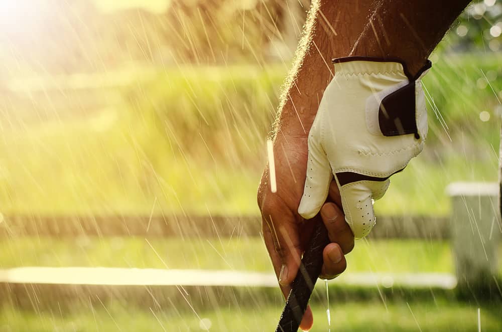 The hands of golfers are holding golf clubs by the wet rain