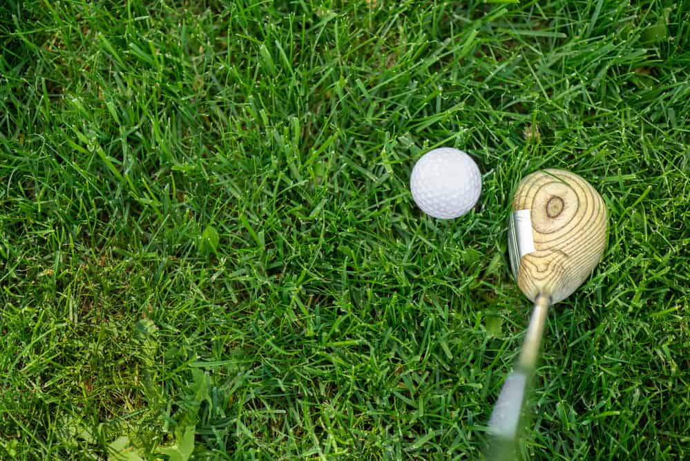 Top view of golf club and ball on green grass