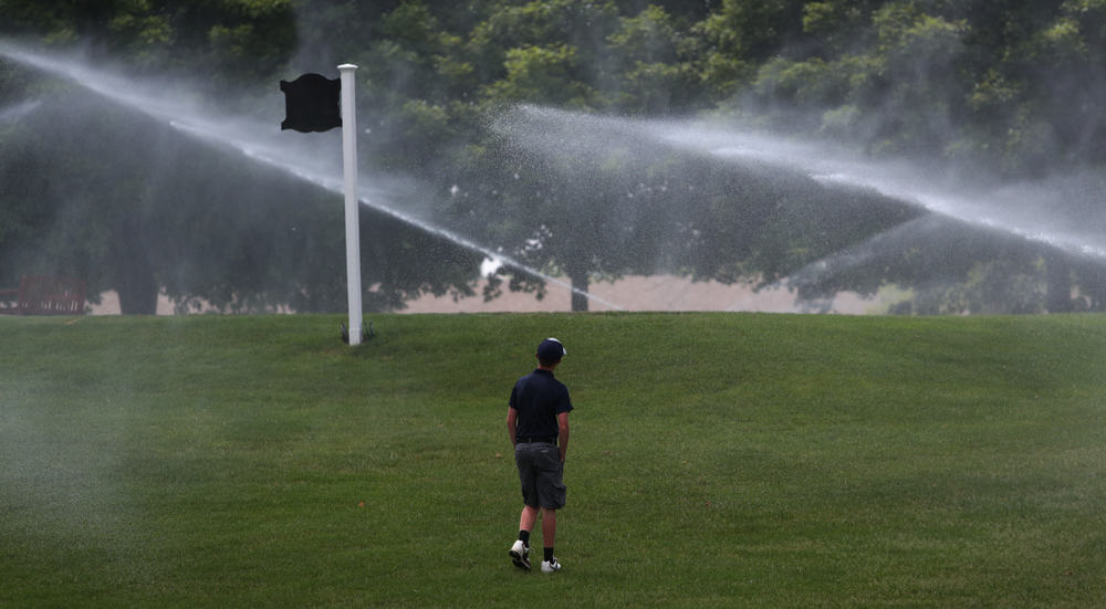 golfer cools off by standing in the mist of a golf course water sprinkler