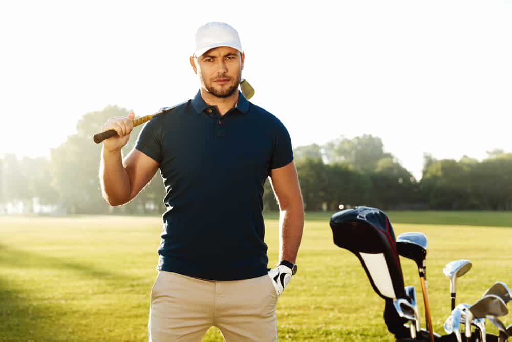 male golfer standing with golf club on a green field