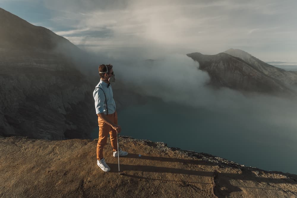 stands on the edge of the crater of volcano in Indonesia with golf club