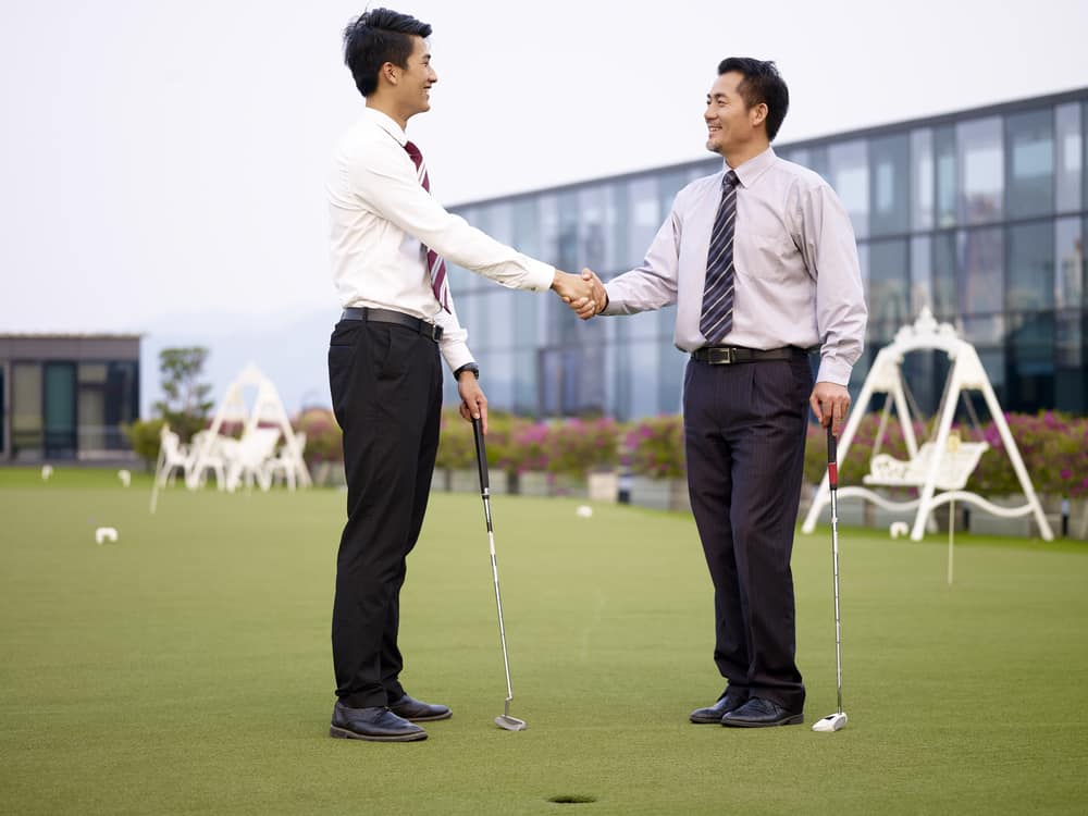 asian corporate executives shaking hands on golf course