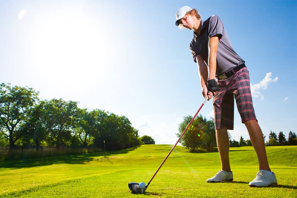 golf player teeing off golf ball from tee box