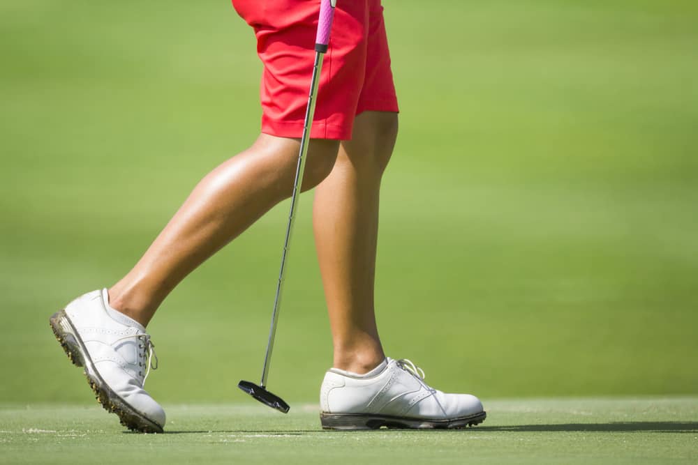 Female golfers walking on green with putter.