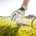 Hand in glove placing golf ball on tee