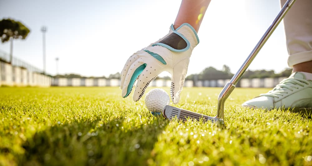 Hand in glove placing golf ball on tee