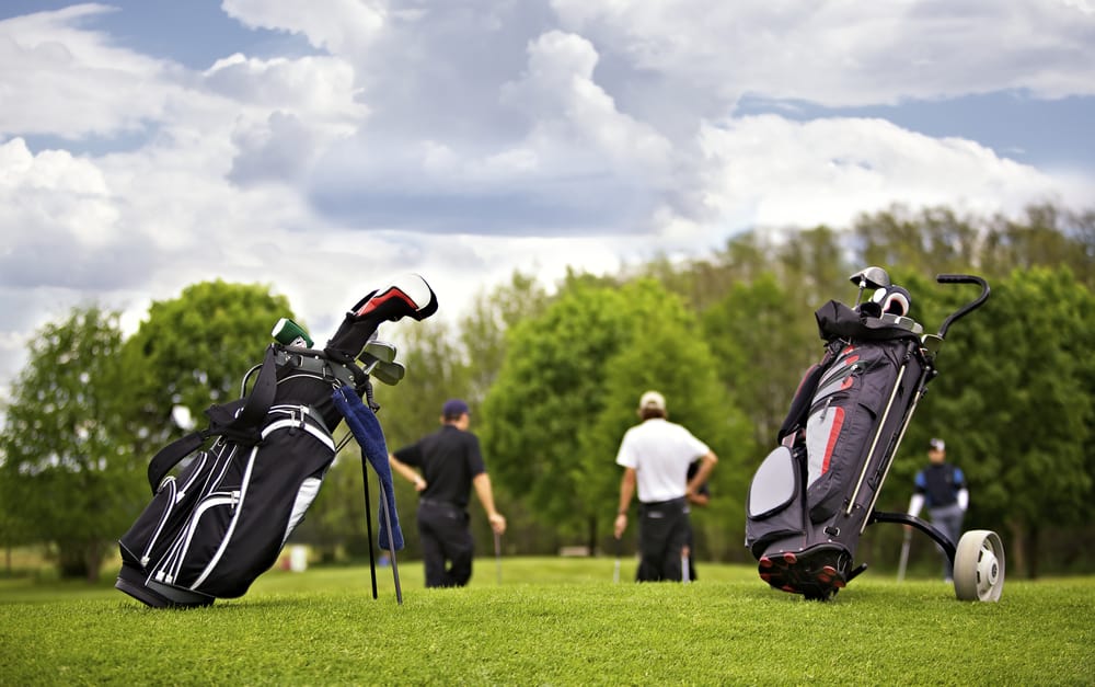 Two golf bags standing in front of a group of golf players putting on green.